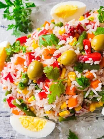Ensalada de Arroz Primavera (Garden Rice Salad) served on a transparent serving platter, topped with olives and hard boiled eggs sliced.
