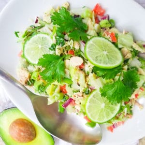 Ensalada de Atun in a white bowl topped with cilantro sprigs and slices of lime.