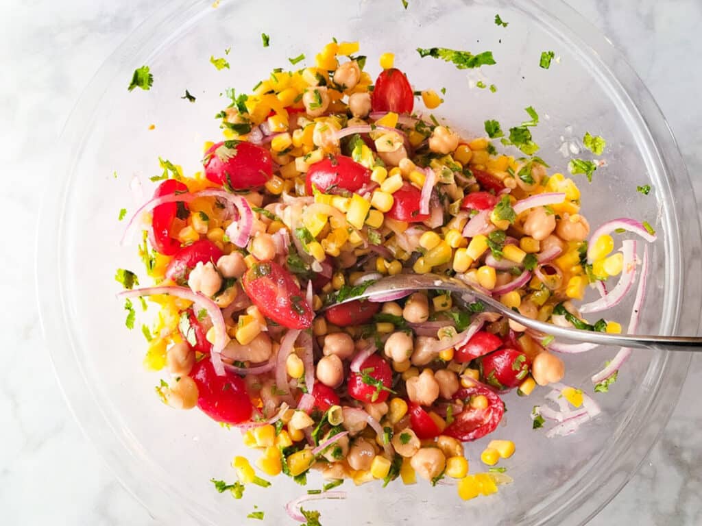 Ensalada de garbanzos mixed in a glass mixing bowl with all the ingredients and lime vinaigrette.