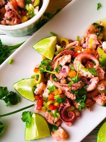 Ensalada de Pulpo (Puerto Rican Octopus Salad) served on a white platter with lime wedges.