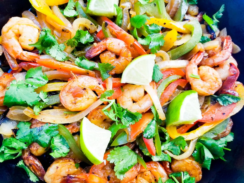 Cooked Shrimp Fajitas in a cast iron skillet, topped with chopped cilantro and lime wedges.