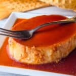 Flan de queso served on a white platter, topped with caramel sauce.