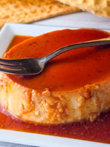 Flan de queso served on a white platter, topped with caramel sauce.
