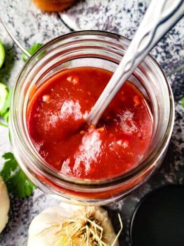 Guava BBQ Sauce (Salsa de Guayaba) in a mason jar with whole heads of garlic beside and lime wedges.
