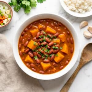 Habichuelas guisadas con calabaza served in a white bowl with a side of white rice and cilantro garnish.