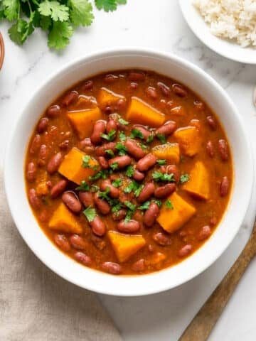 Habichuelas guisadas con calabaza served in a white bowl with a side of white rice and cilantro garnish.
