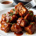 Instant Pot Boneless Pork Ribs served on a white plate with a ramekin full of barbecue sauce on the side and an Instant Pot behind the serving of ribs.
