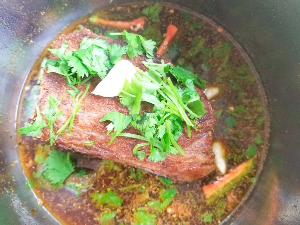 Beef round roast ready to cook inside an instant pot, topped with fresh herbs, spices and garlic.