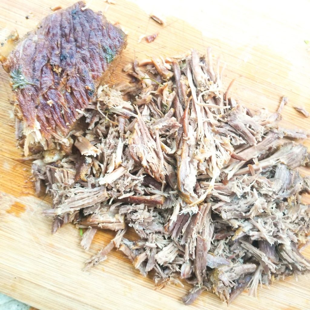 Cooked beef round roast cooked on a wooden cutting board being shredded.
