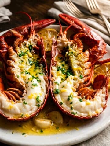 Langosta a la mantequilla, two lobster halves, served on a white platter with lemon wedges.