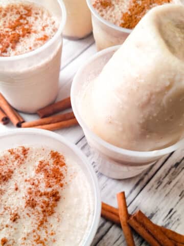 Limber de Leche (Limber de Crema) served in plastic cups, topped with cinnamon and one flipped over inside cup. Cinnamon sticks laying beside limbers.