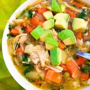 Low Carb Chicken Vegetable Soup made with mixed veggies, including peas, corn, green beans, carrots, onions, fresh chopped garlic and shredded chicken breast in a delicious chicken broth and topped with fresh cilantro and avocado cubes. Served in a white soup bowl.