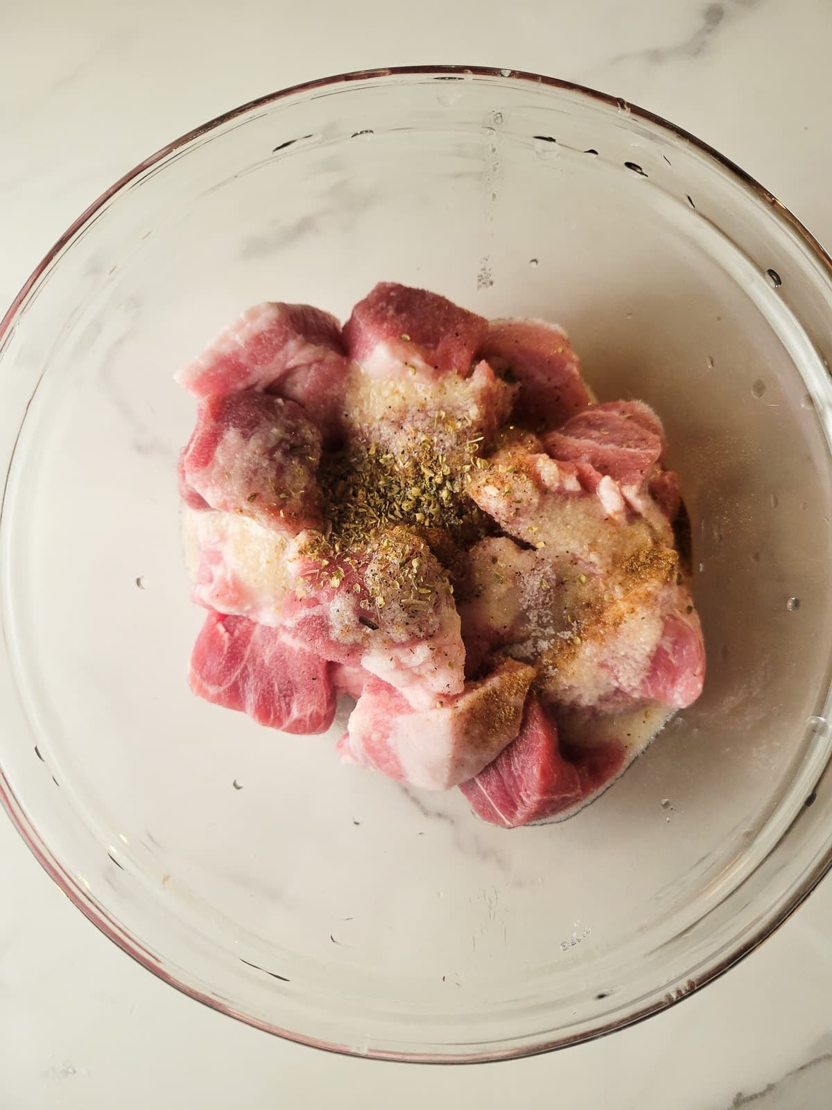 Pork chunks seasoned in a white mixing bowl.