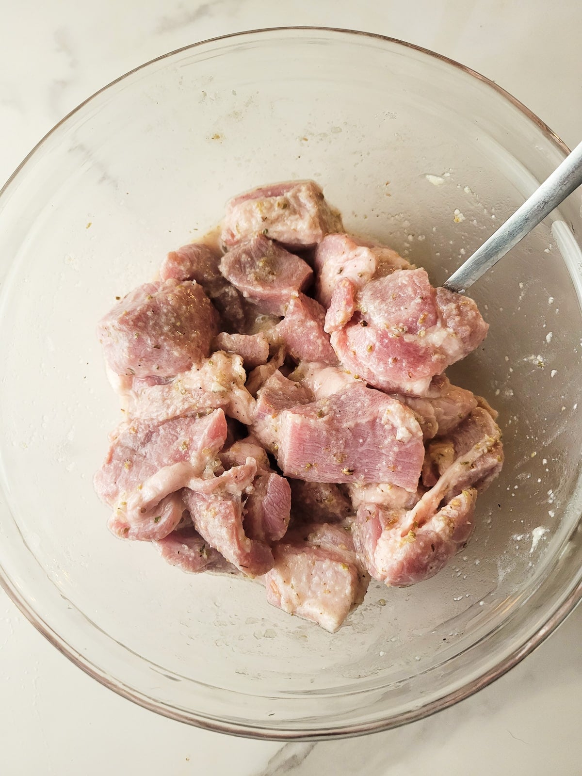 The pork chunks marinating in the seasoning and the sour orange in a white transparent bowl.