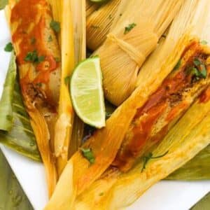 Beef Mexican Tamales served on top of plantain leaves on a white platter.