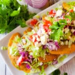 Mexican Empanadas with Green Sauce served on a white platter topped with shredded lettuce, chopped tomatoes, chopped red onions and queso fresco.