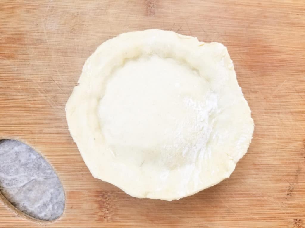 Showing how to place and close a piece of pastry on top of mini turkey filled trays for pot pies.