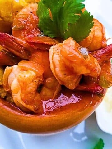 Mofongo con Camarones (Garlic Plantain Mash with Shrimp) served in a pilon (wooden mortar and pestle) and topped with salsa criolla.