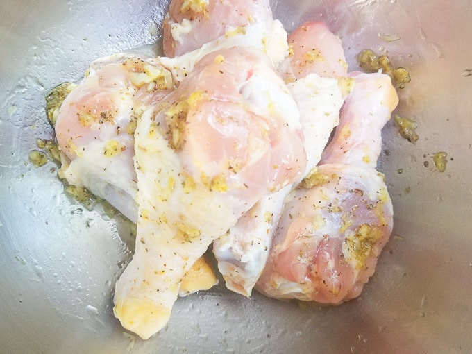 Raw chicken drumsticks in a metal bowl marinating with the garlic marinade.
