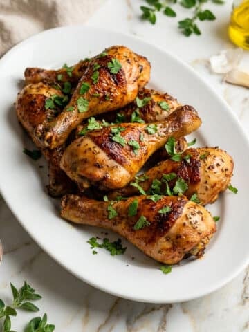 Muslos de pollo (chicken skillet drumsticks) served on a white oval platter.