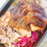 Pernil Asado Puertorriqueno (Puerto Rican Pernil) fully cooked and served in a roasting pan with a side of red onions.