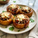Puerto Rican Piononos (Piononos Boricua) served on a cream colored plate, topped with melted cheese and garnished with fresh cilantro.