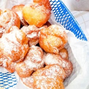 Plantain Puff Puff in a blue wire basket topped with confectioners sugar.
