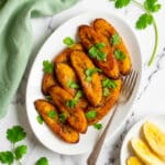 Platanos fritos served on a white platter and a smaller plate with a few raw plantain slices.