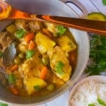 Pollo Guisado (Puerto Rican Chicken Stew) cooked in a caldero pot with a side of white rice and avocado.
