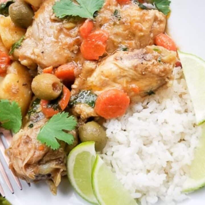 Pollo Guisado (Puerto Rican Chicken Stew) with carrots, potatoes, olives, cilantro, spices in a delicious savory chicken broth served with white rice in a large white deep dish.