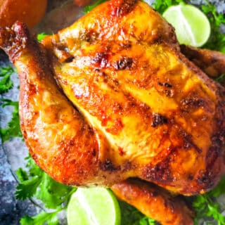 Pollo Rostizado (Rotisserie Chicken) served on a transparent platter with lime wedges and cilantro garnish.
