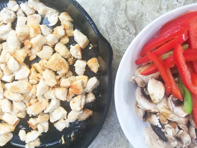 Cooked chicken pieces in a cast iron pan and a side of veggies in a small white bowl.