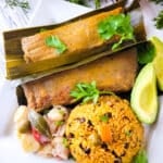 Puerto Rican Pasteles (Pasteles Puertorriquenos) served on a white plate with a side of arroz con gandules, avocado and guineitos en escabeche.