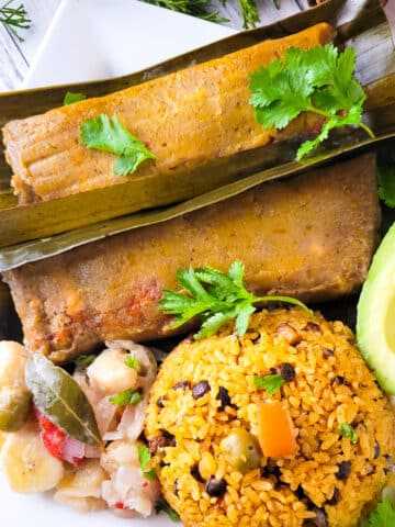 Puerto Rican Pasteles (Pasteles Puertorriquenos) served on a white plate with a side of arroz con gandules, avocado and guineitos en escabeche.