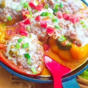 Cooked Puerto Rican Stuffed Peppers in a cast iron skillet, topped with a salsa criolla, monterey jack cheese, chopped scallions and tomatoes.