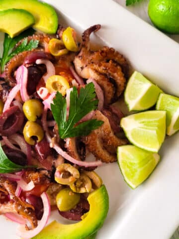 Pulpo a la Parrilla served on a white platter with lime wedges.