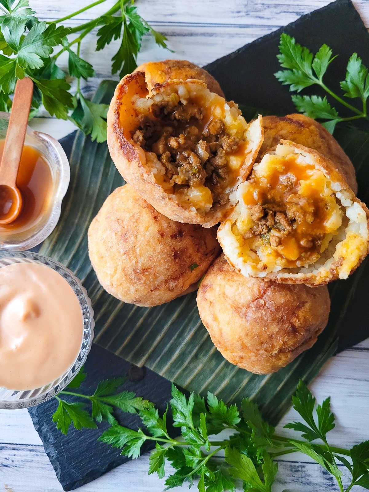 Puerto Rican Rellenos de Papa served on a black serving slate with a side of mayoketchup and hot sauce.
