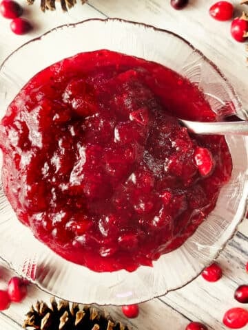Salsa de Arandanos served in a small transparent bowl with fresh cranberries around it and pine cones for decor.