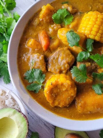 Puerto Rican Sancocho de Res (carne) served in a white bowl with a side of white rice and avocado.