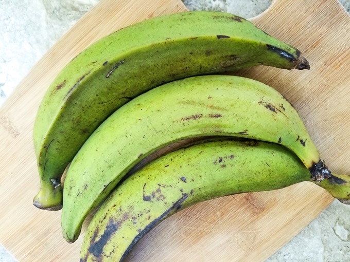 Whole Green plantains on a wooden cutting board.