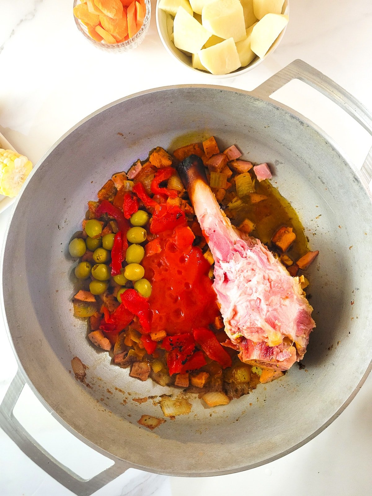 The roasted bell peppers, tomato sauce, olives, and the ham bone added to the pot.