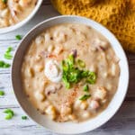 Creamy sopa de papa served in a white soup bowl, topped with chopped scallions and a dollop of sour cream.
