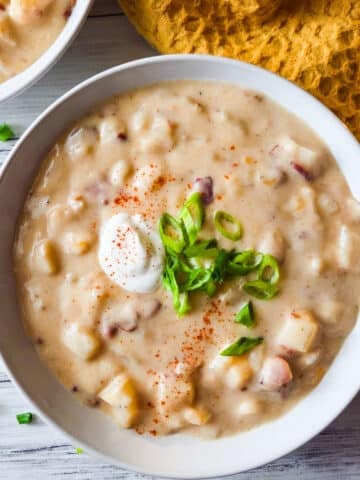 Creamy sopa de papa served in a white soup bowl, topped with chopped scallions and a dollop of sour cream.