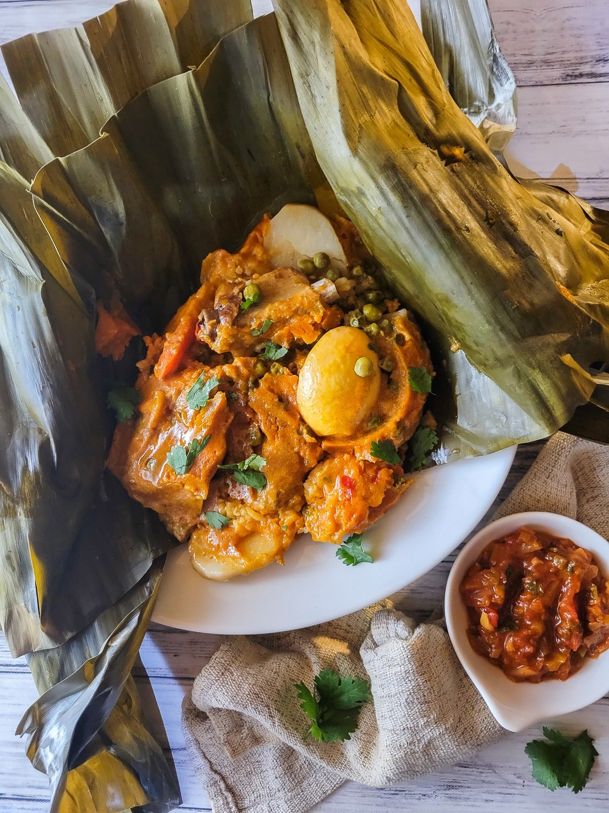 Tamal tolimense served inside banana leaves served on a white plate with a side of Colombian hogao.