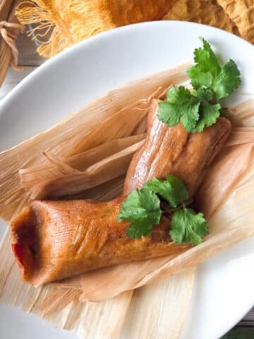 Tamales Cubanos (Cuban Tamales) served in a white platter with other wrapped tamales laying beside it.