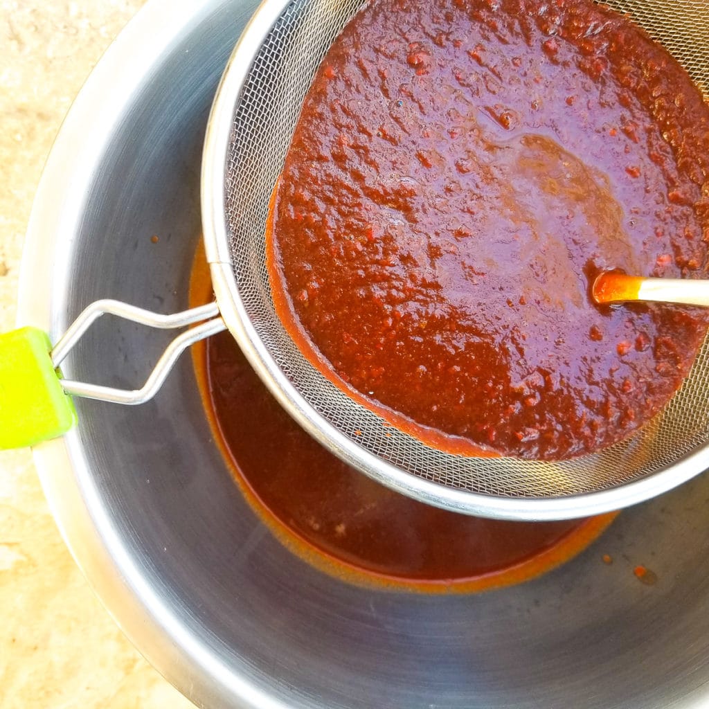 Sauce being strained through a colander for pork tamale filling.