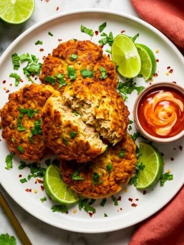 Tortitas de atun served on a white plate with lime wedges and a garlic aioli dipping sauce.