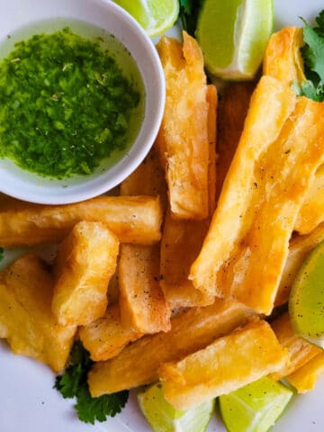 Yuca Frita (Fried Yuca) served on a white plate with a cilantro garlic sauce and lime wedges.
